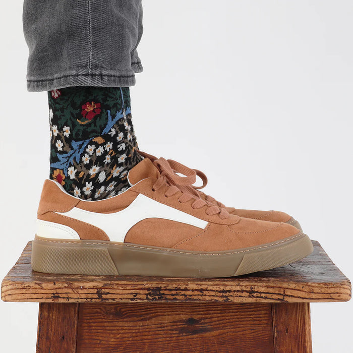 Tan sneakers worn with floral socks on a wooden stool against a white background